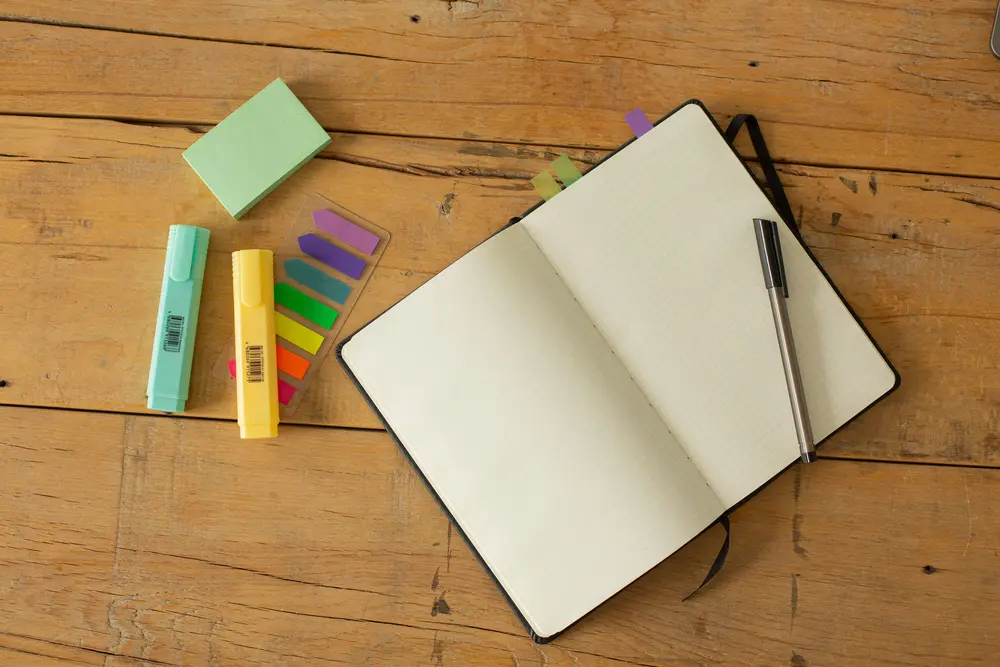 An open book on a desk with a pen sitting on it and other stationery to the side