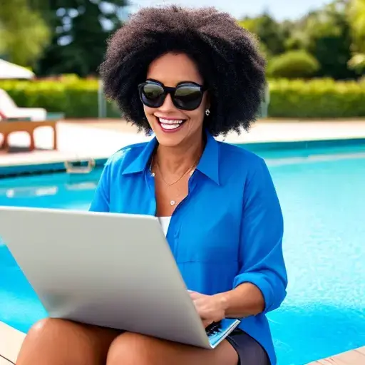 A happy woman sitting next to a swimming pool writing on a laptop computer